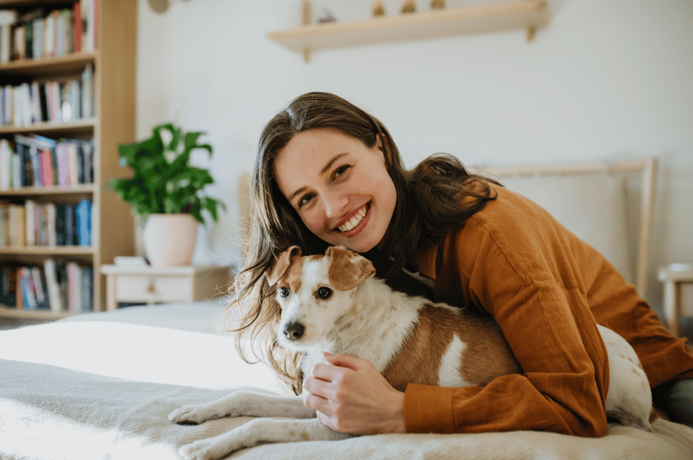 Smiling woman lying on bed hugging small brown and white dog